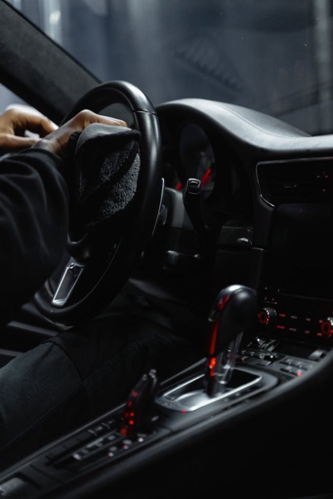 person-in-black-long-sleeves-sitting-on-the-driver-s-seat-while-wiping-the-stirring-wheel-6872585 Close-up of a person cleaning a cars dashboard and steering wheel, focused on interior maintenance.